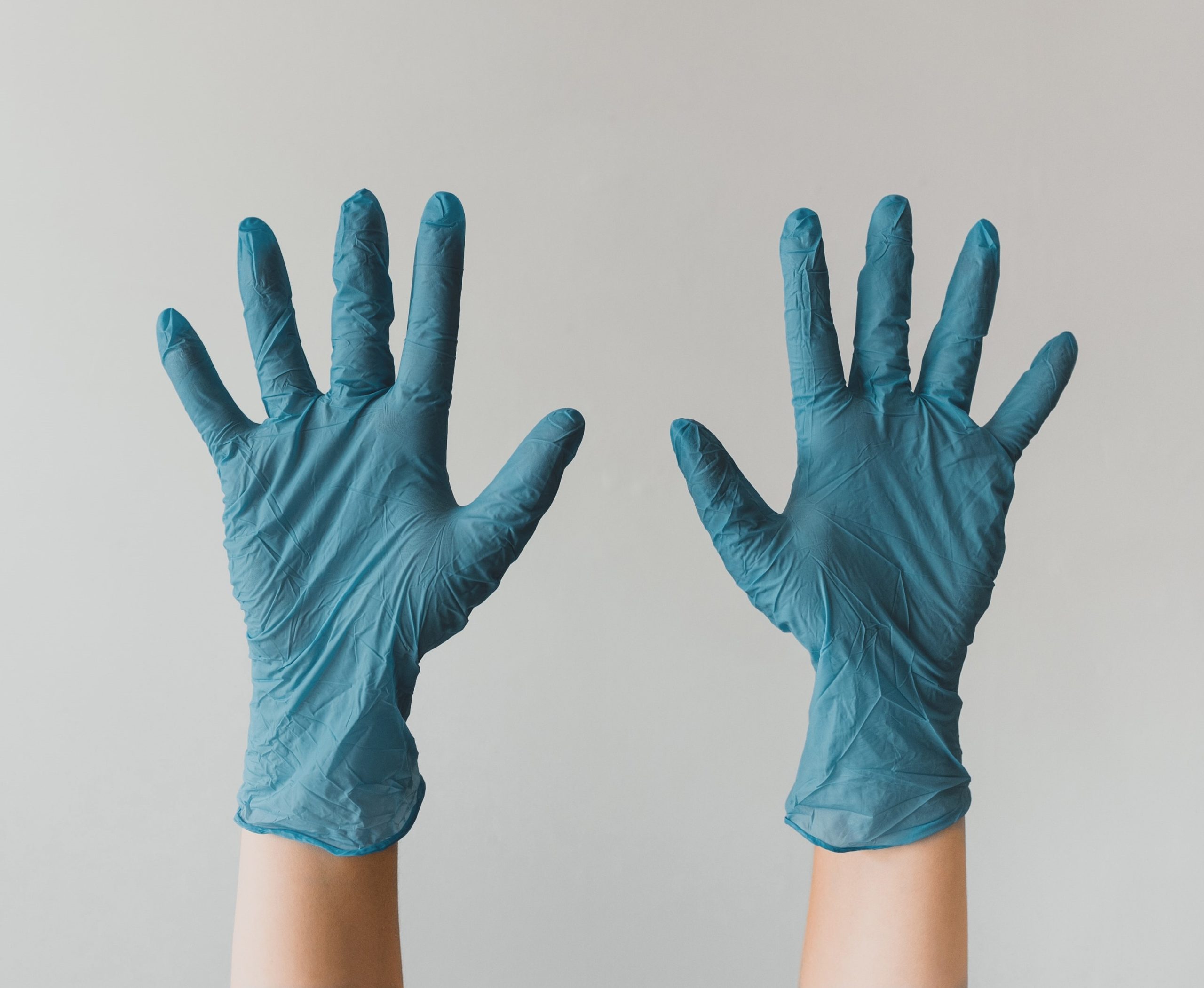 An image of a White person wearing blue medical gloves with their fingers spread wide.